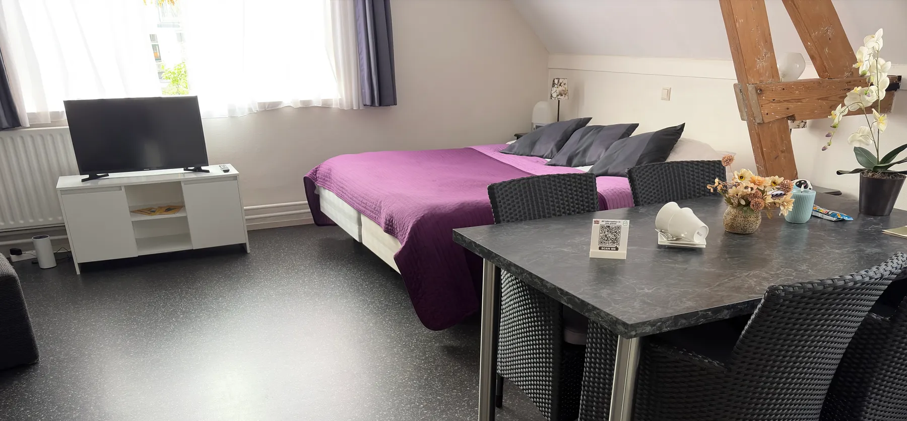 Een B&B-kamer in Arnhem met een tweepersoonsbed, een tafel met stoelen en een QR-kaartje op tafel