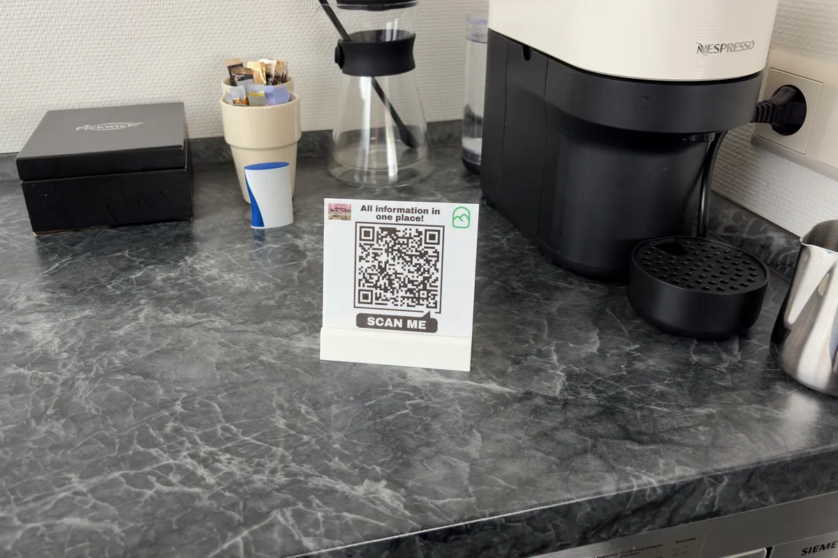 Een QR-kaartje naast een koffiezetapparaat op het aanrecht van een B&B-kamer